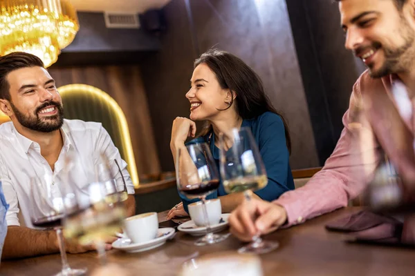 Modern restoranda gülümseyen ve şarap içen bir grup genç arkadaş, neşeli bir sosyal an..