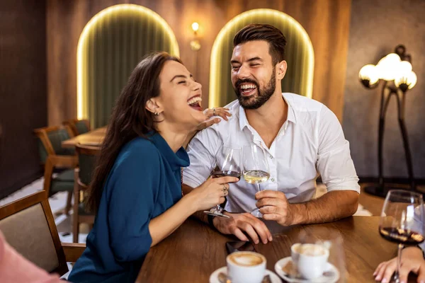 Modern kafede ellerinde şarap kadehleriyle gülümseyen genç bir çift gündelik ve neşeli bir anı paylaşıyor..