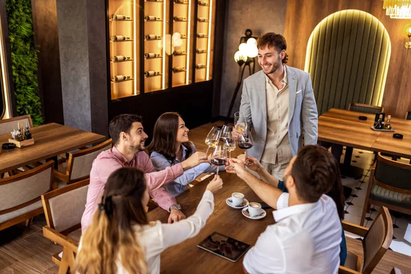 Bir grup genç arkadaş modern kafede kadeh kaldırırken bir adam ayakta duruyor, neşeli sosyal an..