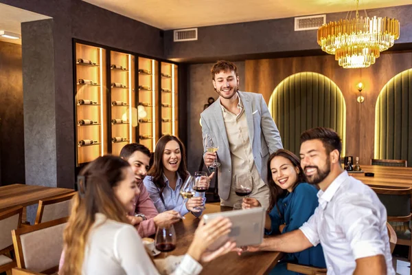 Modern kafede oturan bir grup genç arkadaş video görüşmesi için tablet kullanıyorlar, uzaktan biriyle bağlantı kuruyorlar..