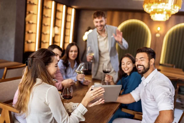 Modern kafede oturan bir grup genç arkadaş video görüşmesi için tablet kullanıyorlar, uzaktan biriyle bağlantı kuruyorlar..