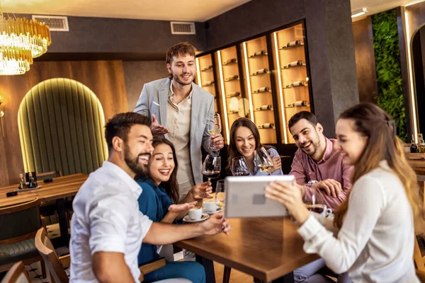 Modern kafede oturan bir grup genç arkadaş video görüşmesi için tablet kullanıyorlar, uzaktan biriyle bağlantı kuruyorlar..