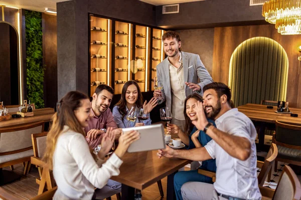 Modern kafede oturan bir grup genç arkadaş video görüşmesi için tablet kullanıyorlar, uzaktan biriyle bağlantı kuruyorlar..