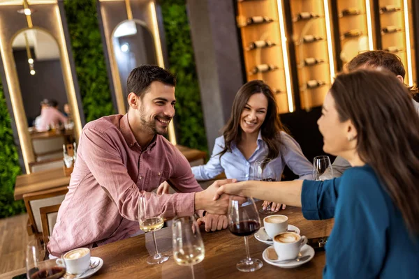 Arkadaşlar izlerken modern kafede gülümseyen genç adam ve kadın el sıkışıyor..
