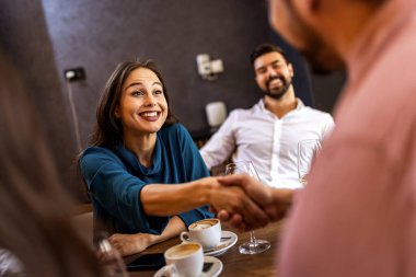 Arkadaşlar izlerken modern kafede gülümseyen genç adam ve kadın el sıkışıyor..