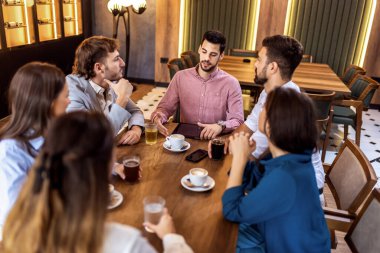 Bir grup genç arkadaş modern kafede birlikte oturup rahatlıyor ve gündelik sohbetin tadını çıkarıyorlar..