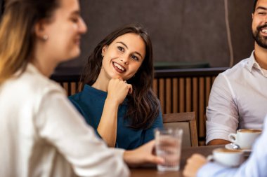 Modern kafede oturup sohbet eden ve içki içen mutlu bir grup genç arkadaş, sıradan bir yaşam tarzı..