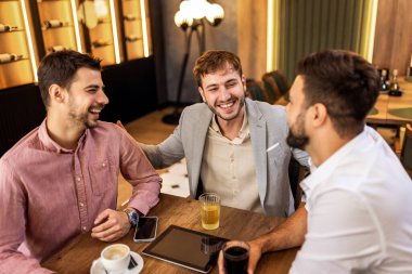 Modern kafede içki ve sohbetin keyfini çıkaran üç adam, gündelik yaşam tarzı anı..