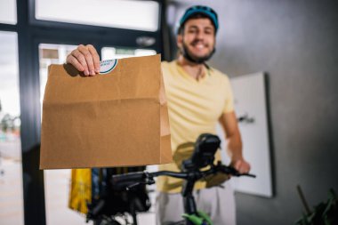 Bisikletli kurye binaya girerken yiyecek paketini elinde tutuyor, hızlı dağıtım, kentsel hizmet, kurye işi, modern şehir yaşam tarzı.