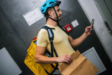 Paket taşıyan kurye akıllı telefondan adresleri kontrol ediyor. Lojistik konsepti, modern servis, kuryelik işi..