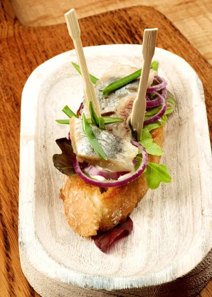 Delicious Fish Tapas with Marinated Sardines, Red Onion and Greens closeup on White Wooden Plate on Wooden background