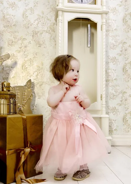 休日のクローズ アップの時計を待っているの下でクリスマス プレゼントに近いふわふわのピンクのドレスかわいい女の子 — ストック写真