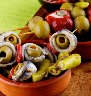 Lezzetli İspanyol Tapas, zeytin kıvrımlı ançüez ve marine edilmiş biberli ahşap kesim tahtasında yakın plan.