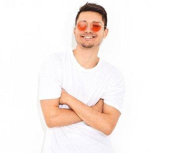 Yakışıklı genç model adam portresi beyaz arka plan üzerinde poz güneş gözlüğü kot elbise ve T-shirt giymiş. Çapraz kollar