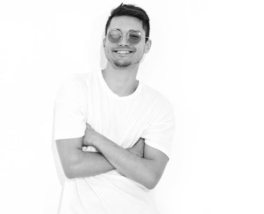 Yakışıklı genç model adam portresi beyaz arka plan üzerinde poz güneş gözlüğü kot elbise ve T-shirt giymiş. Çapraz kollar