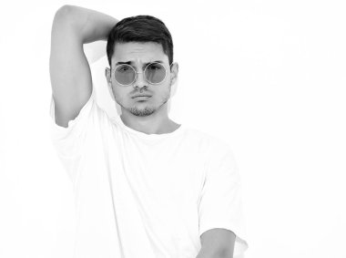 Yakışıklı genç model adam portresi beyaz arka plan üzerinde poz güneş gözlüğü kot elbise ve T-shirt giymiş. Kafasını dokunmadan