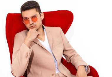 yakışıklı moda şık hipster lumbersexual işadamı modelinin portre Studio beyaz zemin üzerine kırmızı sandalye üzerinde oturan zarif ışık pembe takım elbise giymiş. Metroseksüel
