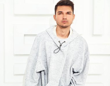 Genç yakışıklı modeli adam portresi dokulu beyaz duvara yakın poz gri rahat Kapşonlu elbise giymiş