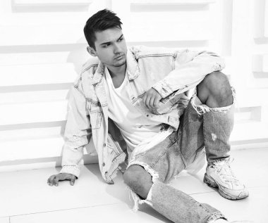 Yakışıklı genç model adam portresi beyaz dokulu duvara yakın oturan kot elbise giymiş