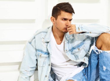 Yakışıklı genç model adam portresi beyaz dokulu duvara yakın oturan kot elbise giymiş