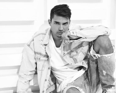 Yakışıklı genç model adam portresi beyaz dokulu duvara yakın oturan kot elbise giymiş
