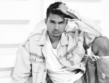 Yakışıklı genç model adam portresi beyaz dokulu duvara yakın oturan kot elbise giymiş