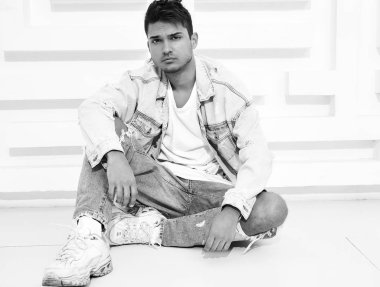 Yakışıklı genç model adam portresi beyaz dokulu duvara yakın oturan kot elbise giymiş