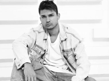 Yakışıklı genç model adam portresi beyaz dokulu duvara yakın oturan kot elbise giymiş