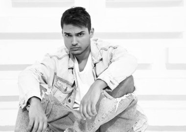 Yakışıklı genç model adam portresi beyaz dokulu duvara yakın oturan kot elbise giymiş