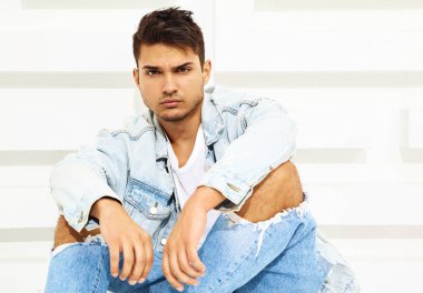 Yakışıklı genç model adam portresi beyaz dokulu duvara yakın oturan kot elbise giymiş