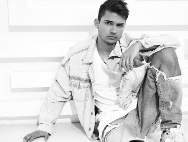 Yakışıklı genç model adam portresi beyaz dokulu duvara yakın oturan kot elbise giymiş