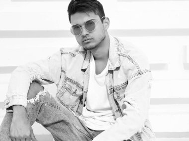 Yakışıklı genç model adam portresi beyaz dokulu duvara yakın oturan kot elbise giymiş
