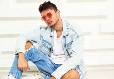 Yakışıklı genç model adam portresi beyaz dokulu duvara yakın oturan kot elbise giymiş