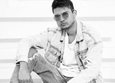 Yakışıklı genç model adam portresi beyaz dokulu duvara yakın oturan kot elbise giymiş
