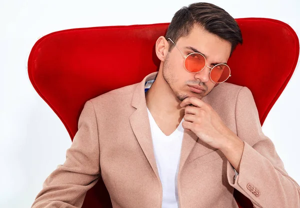 yakışıklı moda şık hipster lumbersexual işadamı modelinin portre Studio beyaz zemin üzerine kırmızı sandalye üzerinde oturan zarif ışık pembe takım elbise giymiş. Metroseksüel
