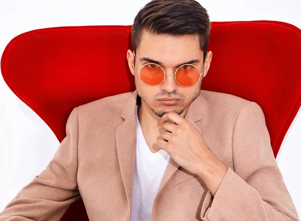 yakışıklı moda şık hipster lumbersexual işadamı modelinin portre Studio beyaz zemin üzerine kırmızı sandalye üzerinde oturan zarif ışık pembe takım elbise giymiş. Metroseksüel