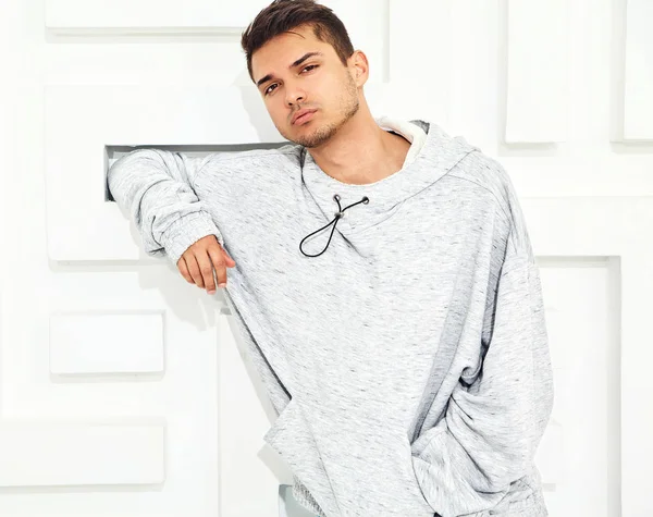 Genç yakışıklı modeli adam portresi dokulu beyaz duvara yakın poz gri rahat Kapşonlu elbise giymiş