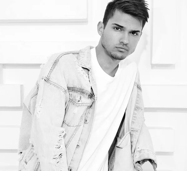 Portrait of young handsome model man dressed in gray casual hoodie clothes posing near textured white wall