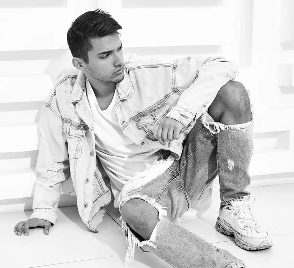 Yakışıklı genç model adam portresi beyaz dokulu duvara yakın oturan kot elbise giymiş
