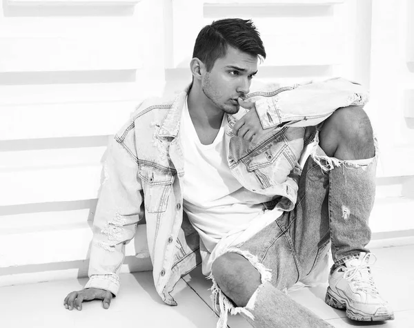 Yakışıklı genç model adam portresi beyaz dokulu duvara yakın oturan kot elbise giymiş