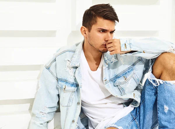 Yakışıklı genç model adam portresi beyaz dokulu duvara yakın oturan kot elbise giymiş