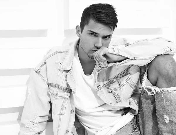 Yakışıklı genç model adam portresi beyaz dokulu duvara yakın oturan kot elbise giymiş