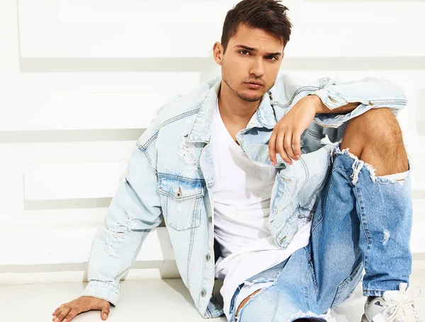 Yakışıklı genç model adam portresi beyaz dokulu duvara yakın oturan kot elbise giymiş