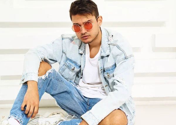 Yakışıklı genç model adam portresi beyaz dokulu duvara yakın oturan kot elbise giymiş