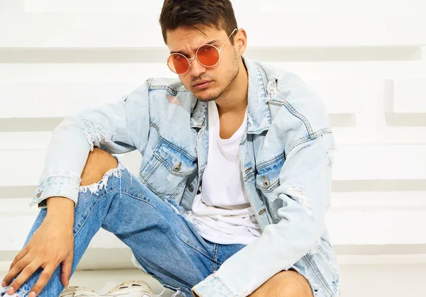 Yakışıklı genç model adam portresi beyaz dokulu duvara yakın oturan kot elbise giymiş