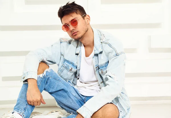Yakışıklı genç model adam portresi beyaz dokulu duvara yakın oturan kot elbise giymiş