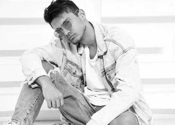 Yakışıklı genç model adam portresi beyaz dokulu duvara yakın oturan kot elbise giymiş