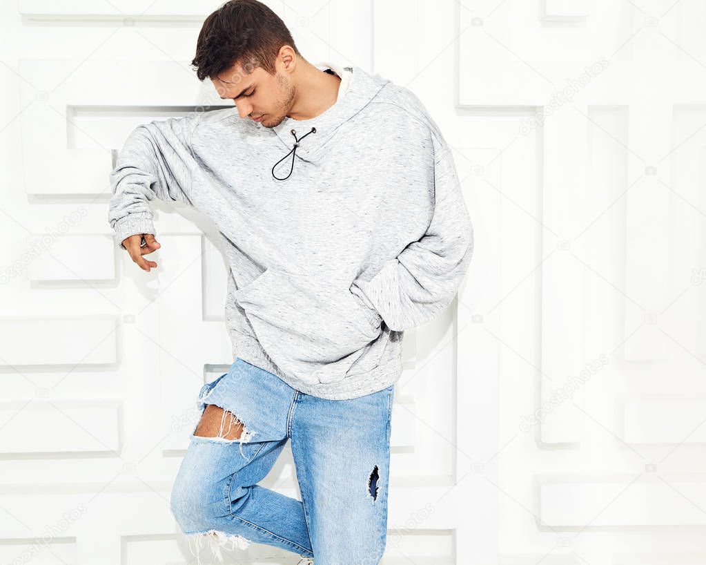 Portrait of young handsome model man dressed in gray casual hoodie clothes posing near textured white wall