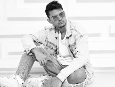 Yakışıklı genç model adam portresi beyaz dokulu duvara yakın oturan kot elbise giymiş