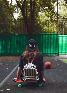 Plastik turuncu penny shortboard şapkalı asfalt üzerinde oturan genç kız